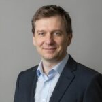 Портрет уверенного российского бизнесмена с дружелюбным взглядом на размытом нейтральном фоне для рекламы Музмейкер